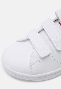 Λευκό sneaker με λείο συνθετικό άνω μέρος, ρυθμιζόμενες ιμάντες από βέλκρο και τρύπες στα πλάγια για αναπνοή.