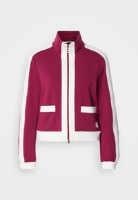 Ζακέτα με φερμουάρ σε βουργουνδί χρώμα, με λευκές ρίγες στο πλάι, ψηλό γιακά, δύο μπροστινές τσέπες και πλεκτά τελειώματα στα μανίκια. Μαλακό ύφασμα με λεία υφή.