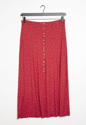 Jupe midi rouge à pois blancs, fermeture à boutons sur le devant, suspendue à un cintre noir sur un fond blanc.
