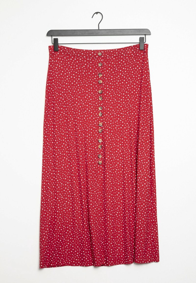 Jupe midi rouge à pois blancs, fermeture à boutons sur le devant, suspendue à un cintre noir sur un fond blanc.