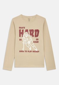 Μπεζ μπλουζάκι μακρύ μανίκι από βαμβάκι, με γραφικό ενός παίκτη χόκεϊ και το κείμενο "SKATE HARD OR GO HOME" σε κόκκινο χρώμα.