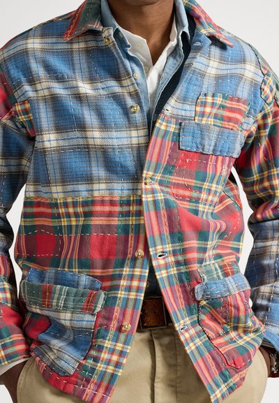 Πολύχρωμο πουκάμισο-μπουφάν με καρό μοτίβα σε μπλε, κόκκινο και πράσινο, με κουμπιά στο μπροστινό μέρος, δύο τσέπες και εμφανείς λεπτομέρειες ραφής.