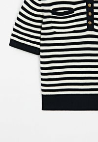 Randig kortärmad tröja i svart och kräm, med ficka och knappslå. Stickad textur med ribbat nederkant och ärmslut.