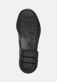 Suela de goma negra de un zapato con patrones de agarre texturizados y logo de la marca, mostrada sobre un fondo blanco.
