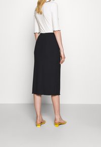 Černá midi sukně s vlnitým lemem, spárovaná s bílým topem s rukávy do lokte a černými lemy. Doplněno žlutými sandály na podpatku.