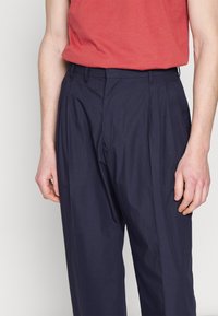 Marinblå plisserade byxor i lätt tyg, med en klassisk design och rak passform samt sidofickor.