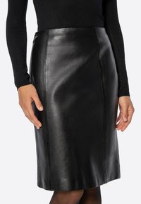 Czarna skórzana ołówkowa spódnica o gładkiej fakturze, długości do połowy uda, z subtelnymi szwami bocznymi. Zestawiona z dopasowaną czarną bluzką.