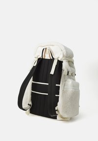 Backpack with plush white fleece top, black fabric body, adjustable straps, side pocket, and white accents. Features sturdy hardware.