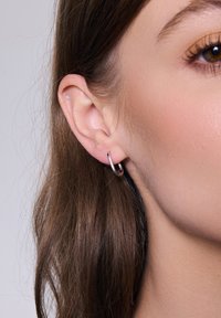 Kolczyk w formie obręczy ze srebra sterlingowego z polerowanym wykończeniem, zwisający z płatka ucha. Prosty okrągły design, średniej wielkości, lekki i smukły.