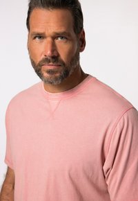 T-shirt a girocollo di colore rosa chiaro, realizzata in tessuto morbido, con maniche corte e dettagli di cucitura rinforzata sul collo.