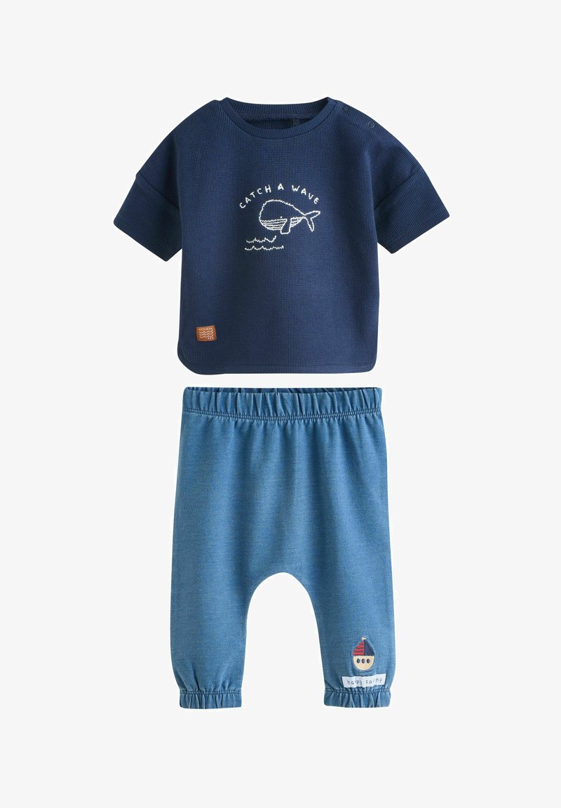 Marineblaues kurzärmeliges Oberteil mit Wal und "Catch a Wave" Text, kombiniert mit blauen Hosen mit elastischem Bund und kleinem Segelboot-Aufnäher.