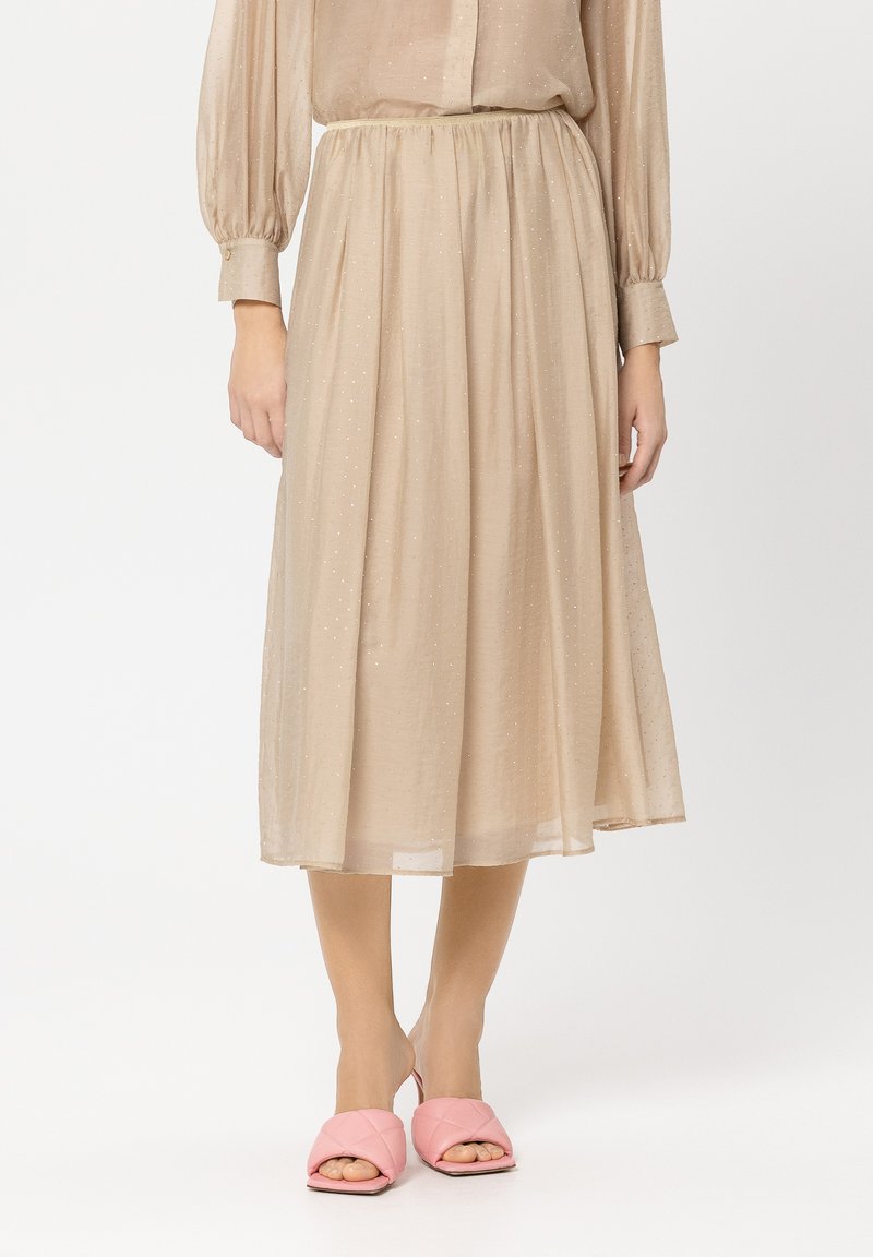 Beige, plissierter Midirock aus leichtem Stoff mit subtilen Glitzerakzenten, kombiniert mit pinken, gesteppten Slip-On-Sandalen.