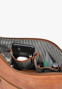 Innenraum einer Ledertasche mit schwarz-weiß gestreiftem Futter. Enthält Fächer für ein Telefon, eine Wasserflasche, AirPods und weitere kleine Gegenstände.