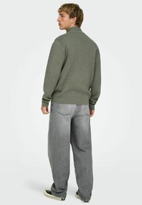 Grijze gebreide trui met opstaande kraag, gedragen met losse grijze spijkerbroek en zwarte sneakers, met een eenvoudig, getextureerd ontwerp.