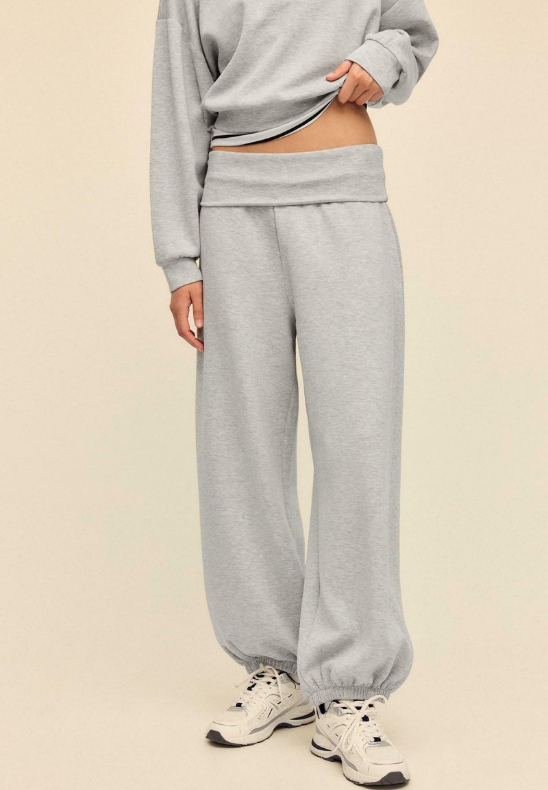 Gray sweatpants with a tapered cuff, made from soft fabric. Features a wide waistband, paired with a long-sleeve top and white sneakers.