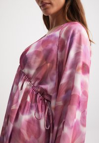 Abito fluido in tessuto trasparente caratterizzato da una combinazione di tonalità rosa e viola, con vita arricciata e maniche lunghe e ampie.