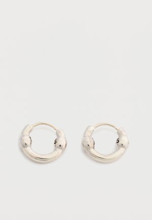 Coppia di piccoli orecchini a cerchio in argento con un design leggermente spesso e arrotondato e una finitura liscia e lucida su uno sfondo chiaro.