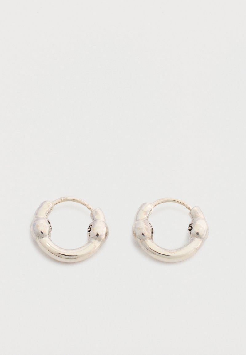 Ζευγάρι μικρών ασημένιων σκουλαρικιών κρίκων με ελαφρώς χοντρό, στρογγυλεμένο σχέδιο και λεία γυαλιστερή επιφάνεια σε ανοιχτό φόντο.