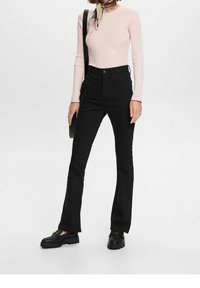 Jeans noirs évasés à taille haute, portés avec un top côtelé à manches longues rose clair. Complétés par des chaussures noires épaisses et un sac assorti.