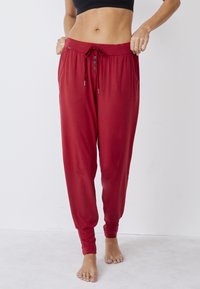 Rode joggingsbroek gemaakt van een zachte, lichte stof. Beschikt over een elastische tailleband met een trekkoord, knopdetail en geribde manchetten.