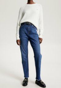 Witte kabelgebreide trui, hoogstwaisted blauwe jeans met rafelige randen en zwarte instappers met een zilveren gesp. Eenvoudige en casual uitstraling.