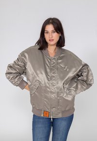 Błyszcząca kurtka bomberka w jasnoszarym kolorze z prążkowanymi mankietami i dołem. Posiada boczne kieszenie, zamek błyskawiczny oraz przeszycia z przodu.