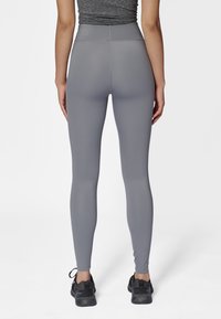 Grå högmidjade leggings av mjukt, elastiskt material, med en kroppsnära design och sömlös baksida samt subtil märkning på midjebandet.