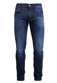 Jeans de mezclilla azul oscuro con corte ajustado. Presenta bolsillos frontales, un bolsillo para monedas y un logotipo de marca distintivo cerca de la cintura.