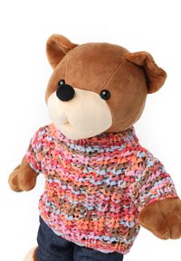 Mjukisdjur i form av en björn som bär en flerfärgad stickad tröja i rosa, blå och orange toner samt jeans. Kropp och ansikte är av mjukt brunt tyg.