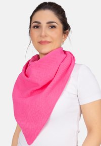 Écharpe en tissu tissé rose avec une finition texturée, disposée en forme triangulaire, portée sur un T-shirt blanc, mettant en valeur sa couleur vive.