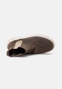 Bota de tobillo de gamuza marrón con paneles laterales elásticos y una suela de goma blanca gruesa. Punta redonda con superficie texturizada y detalles de costura.