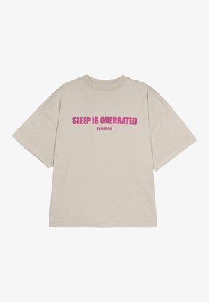 Bežová voľná tričko vyrobené z bavlny s krátkymi rukávmi. Obsahuje výrazný ružový text s nápisom "SPÁNOK JE PRECEŇOVANÝ" a "PEGADOR" pod ním.