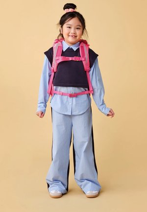 Blue striped shirt under a black sleeveless top, paired with loose light blue pants. Notable pink straps on the top. Light background.