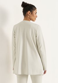 Ljusbeige långärmad tunika i mjukt material med rak skärning, rund halsringning och något längre bak.