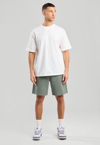 White cotton t-shirt with short sleeves paired with green cotton shorts. Model wears white sneakers and white crew socks. Plain design.