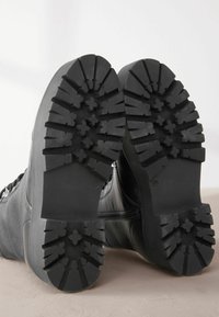Czarne skórzane buty trekkingowe z teksturowanymi gumowymi podeszwami. Podeszwy mają głębokie bieżniki i wyraźne rowki zapewniające przyczepność i trwałość.