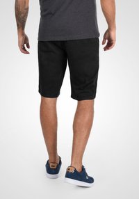 Shorts en coton noirs avec poches latérales, coupe décontractée et texture lisse. Associés à des chaussures en daim bleu avec un accent beige.