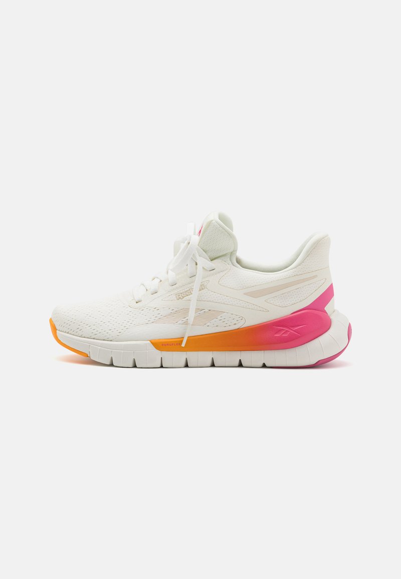 Zapatilla deportiva blanca con parte superior de malla, acentos en degradé de naranja y rosa en la suela, suela de tracción gruesa y cordones blancos.