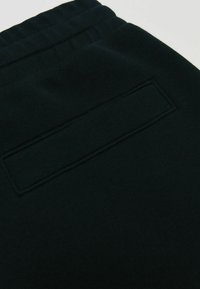 Čierne teplákové nohavice so štruktúrovanou tkaninou, elastickým opaskom a obdĺžnikovou náprsnou vreckom na zadnej strane.