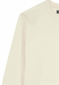 Chemise à manches longues crème, fabriquée en coton doux. Présente un col rond et une texture lisse avec des détails de couture minimes le long des coutures.