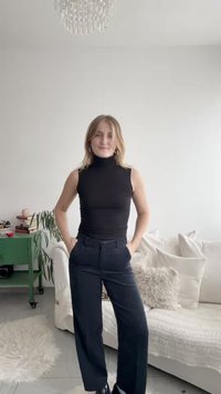 Črna brezrokavnica z visokim ovratnikom, združena s temno modrimi širokimi hlačami z visokim pasom. Modni dodatki vključujejo obročaste uhane, postavljene na svetli podlagi.