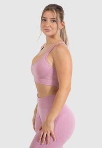 Sujetador deportivo rosa con diseño de escote en V y tirantes anchos, combinado con leggings de cintura alta que presentan acentos texturizados. Tela suave y elástica.