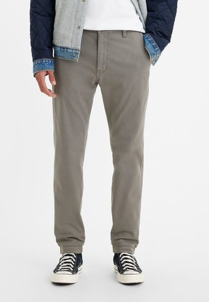 Chinos en coton kaki avec une coupe droite, dotés de poches avant et d'un design épuré. Assortis à des baskets noir et blanc.