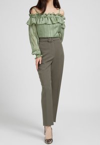 Blusa verde senza spalle con volant, maniche trasparenti; pantaloni olive a vita alta e su misura; tacchi a punta con stampa leopardata.