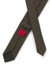 Brown herringbone tie made of textured fabric. Features a red label with "HUGO" and a black lining at the narrow end.