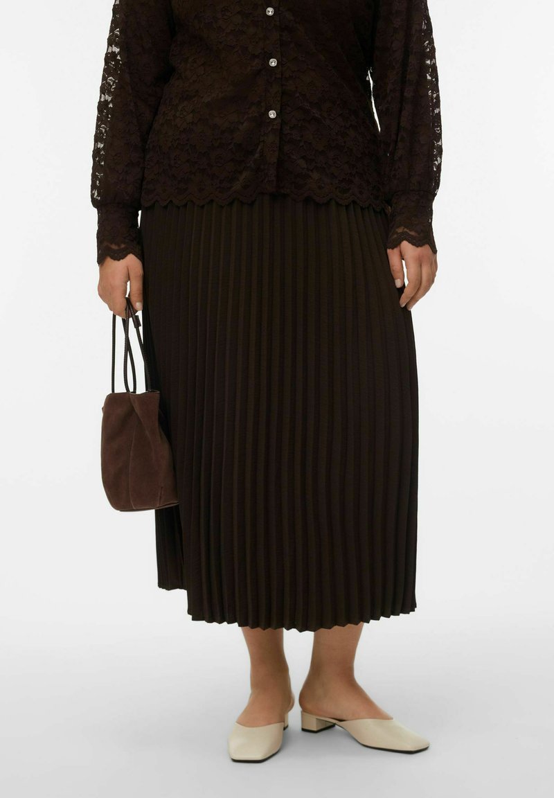 Blouse en dentelle marron foncé à manches longues avec ourlet festonné, jupe midi plissée marron foncé, mules crème et petit sac à main en suède marron.