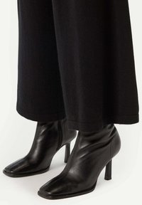 Svarta läder ankelstövlar med spetsig tå och hög klack, med en slät yta och en dragkedja på sidan.