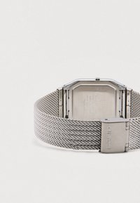 Orologio Casio argento con cassa rettangolare, cinturino a maglia, componenti metallici e retro inciso. Presenta una superficie lucida e una trama a maglia dettagliata.