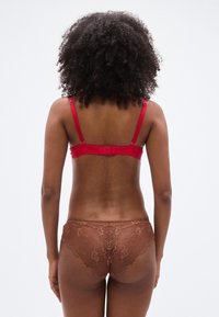 Soutien-gorge rouge avec bretelles réglables et fermeture à agrafes, assorti à une culotte en dentelle marron ornée de motifs floraux. Vue de dos mettant en valeur le design général.