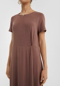 Brąsowy krótki rękaw sukienka z miękkiego materiału, z detalem w postaci skręconego węzła w talii oraz wyprofilowanym dekoltem.